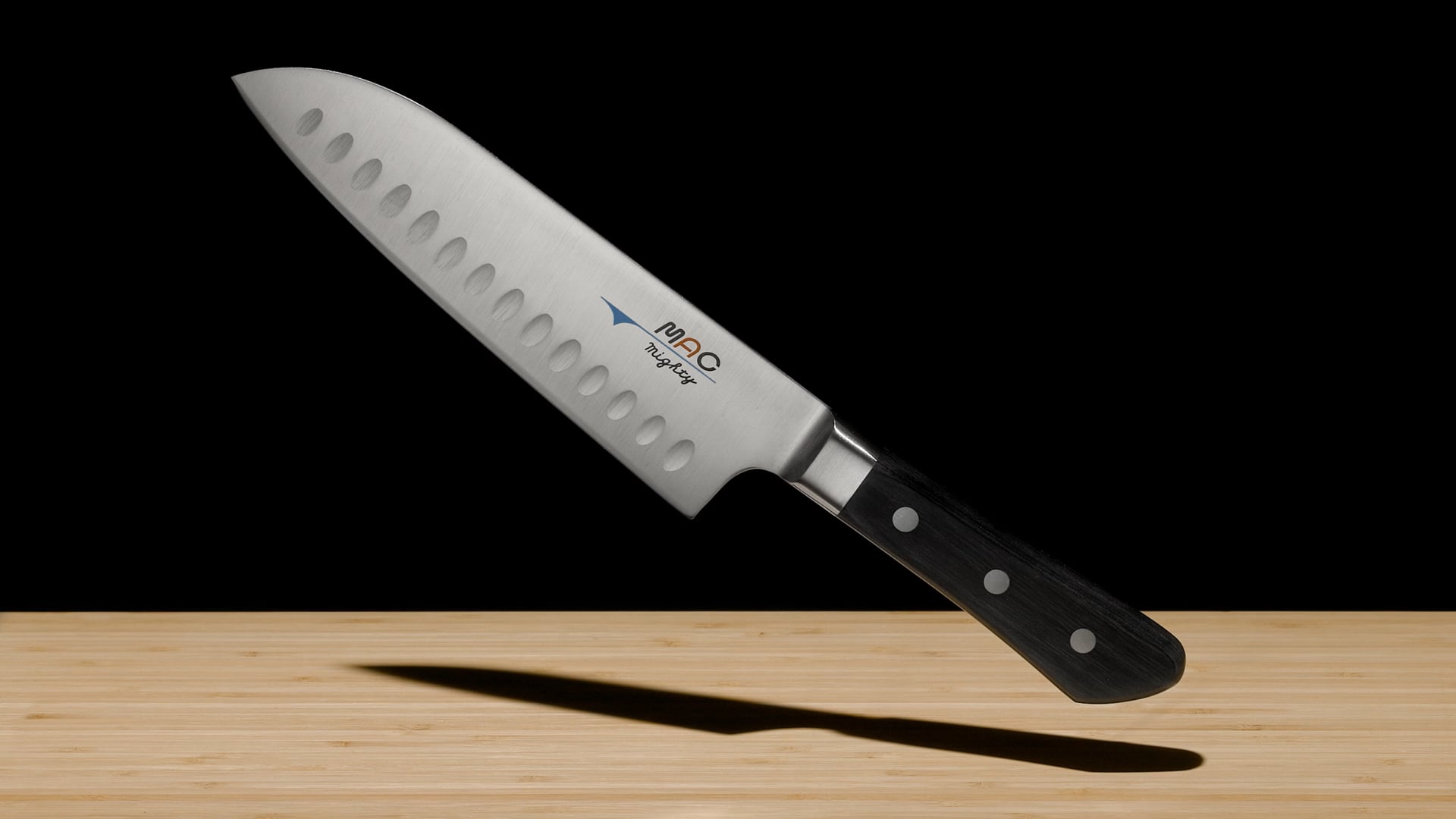 A dramatic marketing video gradually revealing a MAC MSK-65 Japanese Santoku Knife with taiko drums for sound.  First the box is shown, then various details and features of the knife, and finally a full reveal floating and rotating above a bamboo cutting board